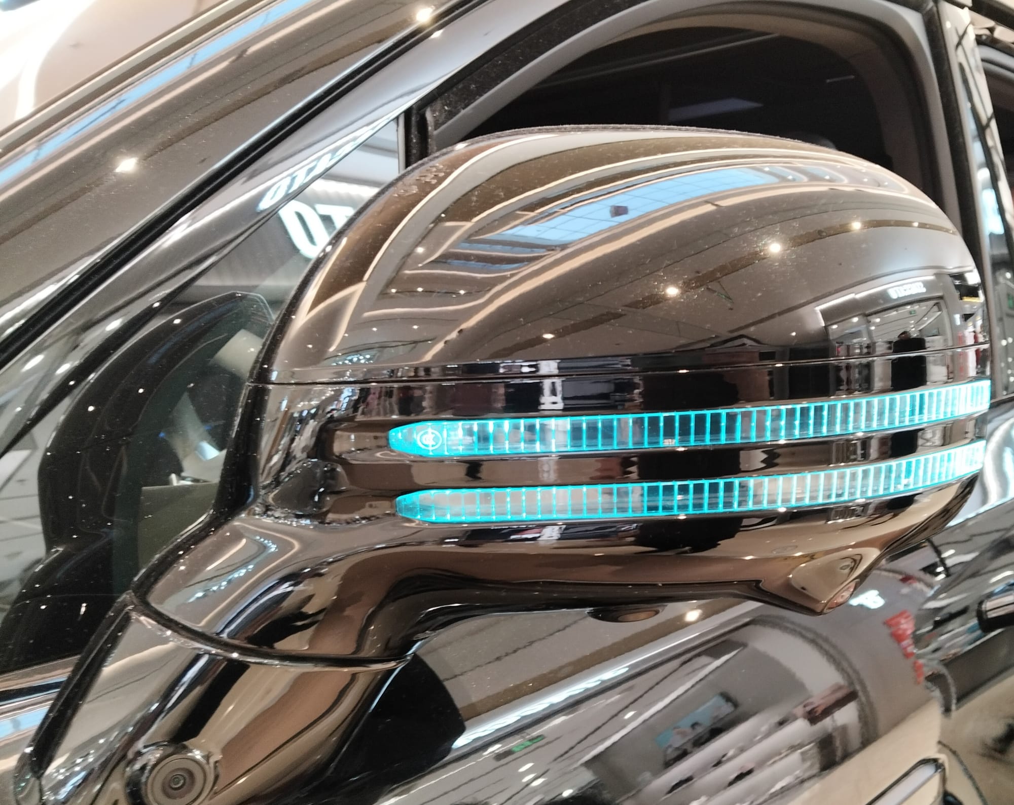 Left side-view mirror of a car with two rows of turquoise lights facing forward