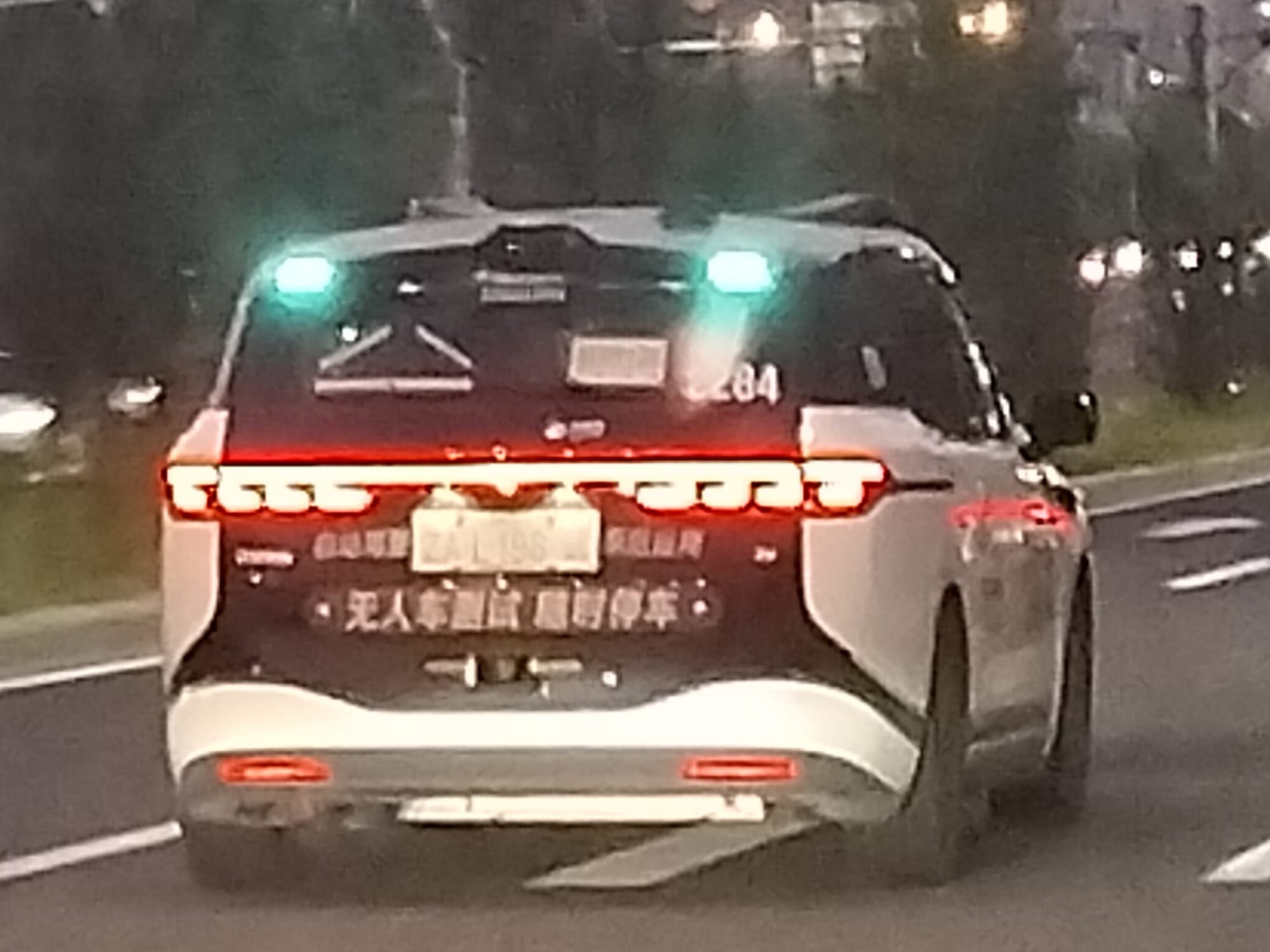 Photo of the rear of a Chinese robotaxi with a blue light at the top right and left corners of the rear windshield.